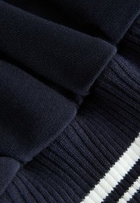 Tela de punto azul marino con secciones texturizadas y lisas, que presenta un dobladillo grueso acanalado con rayas blancas. Vista en primer plano que resalta los detalles.