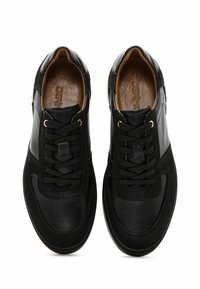 Baskets en cuir noir avec des panneaux lisses et texturés, fermeture à lacets et œillets dorés. L'intérieur présente une doublure beige et un logo embossé.