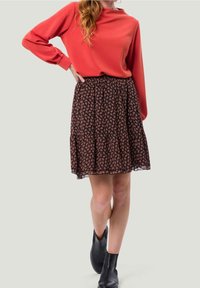 Czerwona bluzka z długim rękawem w połączeniu z czarną spódnicą z kwiatowym wzorem. Spódnica ma rozkloszowany krój i warstwowy dół. Czarne botki za kostkę.