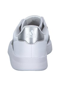 White athletic shoe with a smooth leather upper, padded collar, and metallic silver accent on the heel. Textured rubber sole.