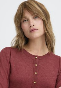 Bordeauxfarbener Cardigan mit Rundhalsausschnitt, strukturiertem Stoff und sechs goldfarbenen Knöpfen auf der Vorderseite. Weicher Strick mit einem dezenten Glanz.