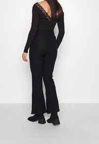 Czarny prążkowany top z długim rękawem, wykończony koronką i głębokim dekoltem na plecach, zestawiony z rozkloszowanymi czarnymi spodniami oraz botkami na słupku.