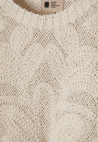 Pull en maille couleur crème avec des motifs texturés détaillés et une étiquette Centralne Muzeum Włókiennictwa w Łodzi au col.