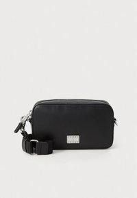 Sort skuldertaske i læder med sølvfarvet beslag, lynlåslukning og justerbar strop af stof. Har en mærket logo-plade på fronten.