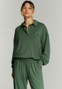 Pullover verde a maniche lunghe con colletto e bottoni decorativi. Presenta un logo ricamato sul petto e una vestibilità comoda.