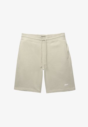 Világos bézs szövetnadrág, puha anyagból készült, rugalmas derékkal, zsinórral és oldalsó zsebekkel rendelkezik, a szegély közelében egy kis logóval.