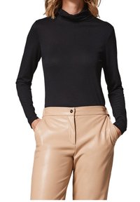 Haut noir à manches longues avec col roulé, associé à un pantalon beige taille haute en cuir synthétique, doté de poches latérales et d'un bouton argenté en guise d'accent.