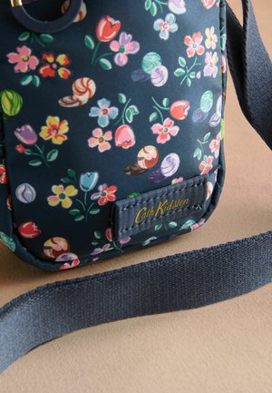 Borsa in stoffa blu navy con motivo floreale, caratterizzata da fiori rosa, gialli e verdi. Include accessori di forma tonda e una tracolla blu. Logo Cath Kidston visibile.