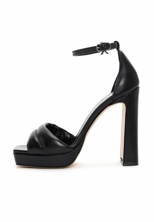 Chaussure à talon haut en cuir noir avec une plateforme épaisse et une bride de cheville, présentant un design courbé élégant et une texture lisse.