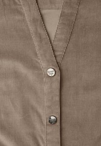 Camicia marrone in velluto a coste con scollo a V, caratterizzata da due bottoni d'argento con la scritta "Street One." Tessuto strutturato e cuciture precise sono ben visibili.