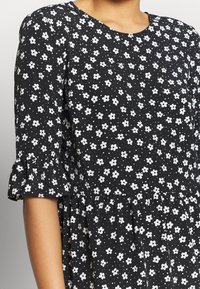Musta kangasmekko, jossa on valkoinen kukkakuosi ja pilkkuja. Ympyräkaulus ja levenevät hihat, virtaava muotoilu, jossa on rypytyksiä vyötäröllä.
