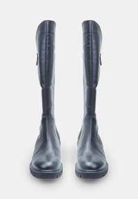 Botas de cuero negras, altas, con puntas redondeadas y suelas de goma gruesa, en posición vertical sobre un fondo blanco.