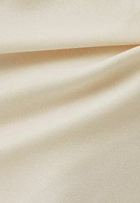 Beige tyg med en mjuk, slät textur, lätt rynkad, och med ett fint vävmönster. Lämplig för kläder eller möbelklädsel.