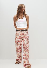Hvid, cropped tanktop med pink tekst, parret med løse bukser med blomster mønster i pink og crema nuancer. Sort bælte og sandaler.