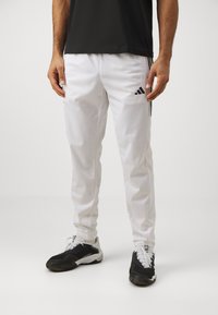 Pantalones deportivos blancos con el logo negro de Adidas, con un corte ajustado y una textura suave. Combinados con zapatillas deportivas en blanco y negro.