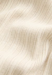 Nahaufnahme eines weichen, cremefarbenen, gerippten Strickstoffs mit sichtbarer Textur und sanften Falten.