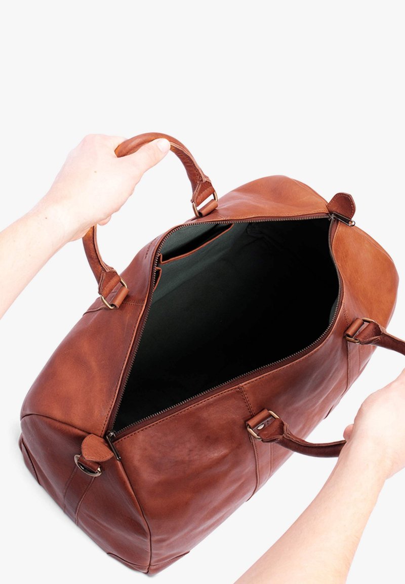 Braune Lederreisetasche mit Reißverschluss oben, zwei Griffen und geräumigem Innenraum aus schwarzem Stoff. Verfügt über Lederakzente und Metallbeschläge.