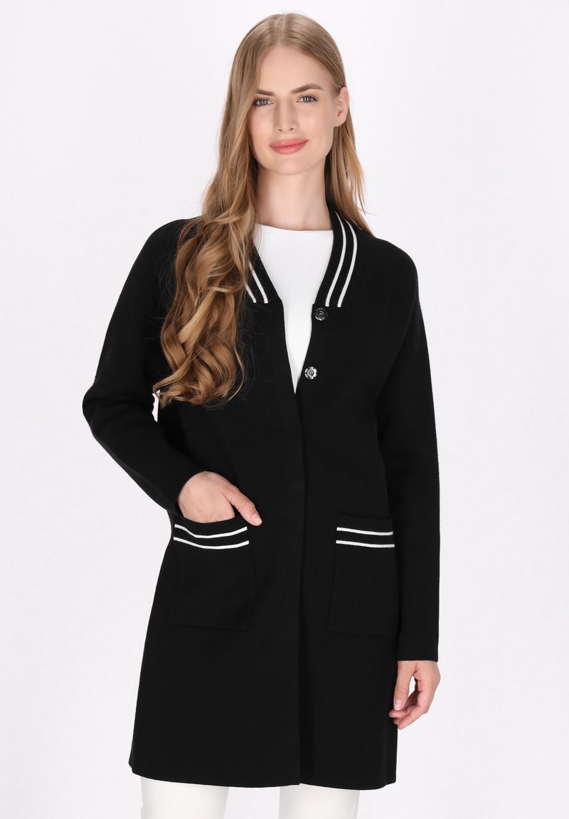 Schwarze Strickjacke mit weißen gestreiften Akzenten an Kragen und Taschen; mit Knopfverschluss und langen Ärmeln, aus einem strukturierten Stoff gefertigt.