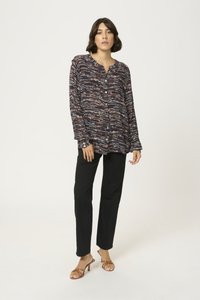 Long, button-up shirt with a multicolored abstract pattern; black pants; brown heeled sandals; smooth fabric with a relaxed fit.