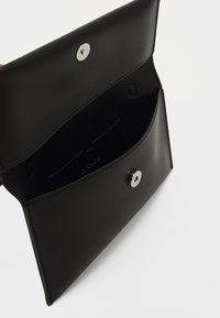 Mustast nahast clutch, millel on sile tekstuur, klõpsuga sulgemine ja sisemine kaardipesa. Minimalistlik disain ilma välisteta embellishments.