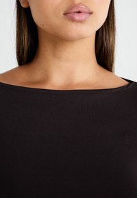 Top nero a maniche corte con scollatura ampia, realizzato in tessuto morbido, caratterizzato da una superficie liscia e dettagli di cucitura minimi.