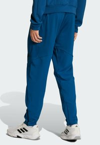 Blaue Sporthose aus leichtem Material. Sie verfügt über schmal zulaufende Beine mit Seitennaht, einen elastischen Bund und schwarze Akzente.