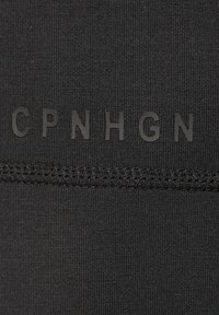 Schwarzer Stoff mit einer glatten, matten Oberfläche, auf dem der erhobene Text "CPNHGN" und horizontale Nahtdetails zu sehen sind. Das Material ist dehnbar und enganliegend.