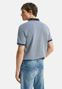 Grijze polo met contrasterende marineblauwe kraag en gestreepte accenten, gedragen met lichtblauwe denim jeans, gezien van achteren.