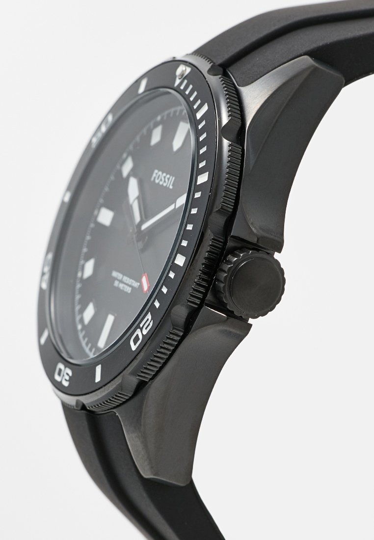 Schwarze Fossil-Uhr mit rundem Ziffernblatt, Gehäuse aus Edelstahl und strukturiertem Gummiband. Weiße Stundenmarkierungen und eine Krone auf der rechten Seite.