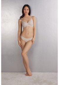 Beige naadloze beha en bijpassende bikini-set, met zachte stof, minimalistisch ontwerp en dunne bandjes, weergegeven tegen een neutrale achtergrond.