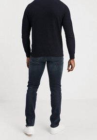 Marinblå texturerad stickad tröja i kombination med mörka denimjeans och vita sneakers. Fokusera på en avslappnad passform och subtila sömnadsdetaljer.