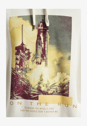 Fehér kapucnis pulóver, amelyen egy rakéta indítását ábrázoló grafikai design található füsttel körülvéve, alatta a "FUTÁSBAN" felirattal és egy sárga téglalappal.