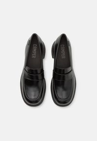 Paire de mocassins en cuir noir avec des bouts ronds et des talons bas, comportant une large bride sur le dessus et des semelles intérieures avec logo.