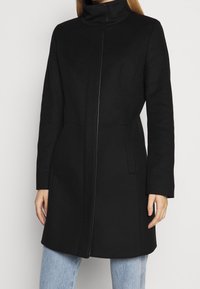 Black wool coat with a high collar, front zipper closure, side pockets, and a tailored fit, featuring a smooth texture and clean lines.