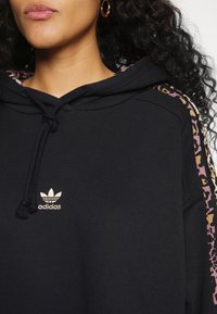 Felpa nera con cappuccio e coulisse, con un piccolo logo dorato Adidas e dettagli in stampa leopardata sulle maniche in rosa e beige.