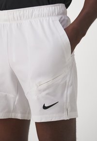 Witte sportshorts met een elastische tailleband, zijzakken en een zwart Nike-logo onderaan links. Glad materiaal en een getailleerde pasvorm.