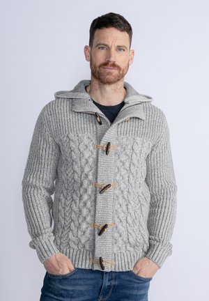 Grey knitted hoodie with a cable pattern, wooden toggle fastenings, and ribbed cuffs. Worn over a dark shirt and blue jeans.