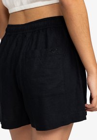 Svart linshorts med elastisk midjebånd og en baklomme med et lite preget hjerte-logo. Glatt tekstur og avslappet passform.