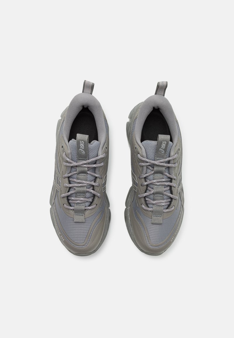 Graue Sportschuhe mit einem Mesh-Obermaterial, gepolstertem Kragen und strukturierten Akzenten. Die Schnürsenkel sind durch eine verstärkte Zunge gefädelt.