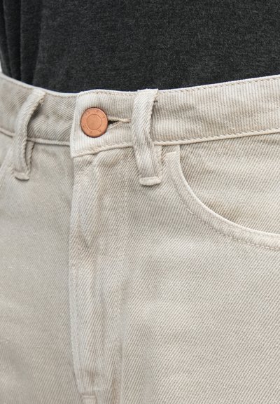 Μπεζ παντελόνι κορντό με ευθεία γραμμή, με κούμπωμα χαλκοκόκκινο κουμπί και εμφανείς ραφές κατά μήκος της μέσης και των τσεπών.