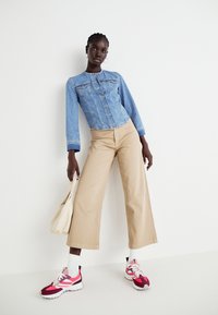 Svetlo modra jeans jakna z gumbi, bež široke hlače in roza športni čevlji. Dodatna oprema: smetana tote torba.