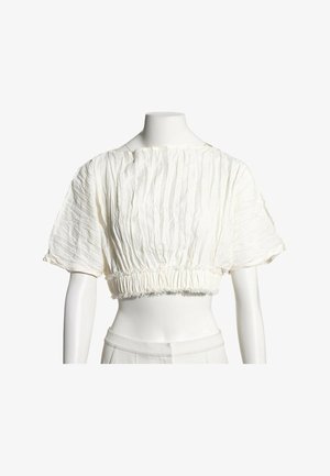 Blouse blanche courte à manches courtes bouffantes avec un détail de tissu froncé à la taille et à l'encolure sur un mannequin.