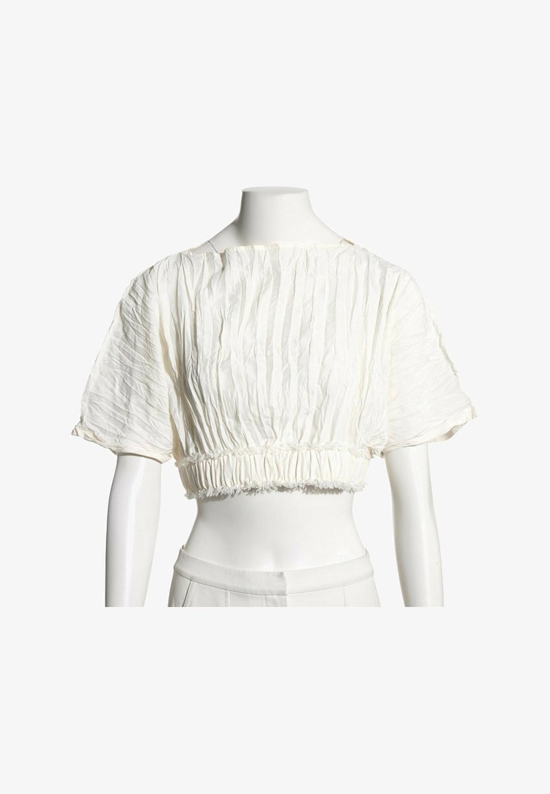 Blouse blanche courte à manches courtes bouffantes avec un détail de tissu froncé à la taille et à l'encolure sur un mannequin.
