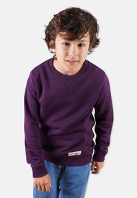 Lila sweatshirt i mjukt material, med standard rund hals och ribbstickade ärmslut, i kombination med blå denimjeans. Märkespatch på fållen.