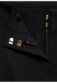 Gros plan d’une fermeture de vêtement noire montrant un bouton, une fermeture éclair partiellement ouverte et deux crochets métalliques dorés avec œillets assortis.