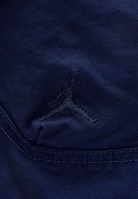Mørkeblå stof med en tekstureret overflade, der har et mørkt broderet Jumpman-logo og synlige syninger langs kanten.