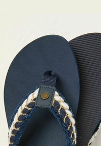 Navy flip-flops with textured dark soles, featuring a braided strap with blue, white, and gold threads, secured by a black metal accent.
