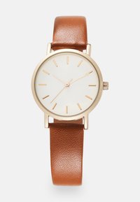 Montre avec un bracelet en cuir brun, un cadran blanc, un cadre doré et de simples marqueurs d'heure dorés. Présente une petite couronne sur le côté.