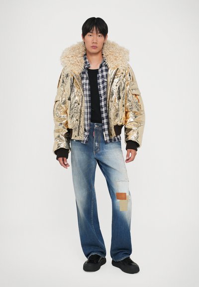 Gouden metallic bomberjack met nepbontkraag, zwarte longsleeve, geruite flanellen overhemd, distressed lichtblauwe denim, zwarte schoenen.
