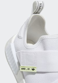 Zapatilla textil blanca con un diseño tipo calcetín, suela de goma y una etiqueta verde con el detalle "NMD_R1" y el logo.